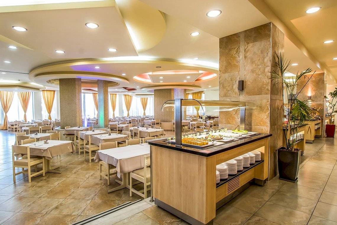 Innenansicht des Restaurants im Pegasos Deluxe Beach Hotel mit vielen Tischen und Stühlen.