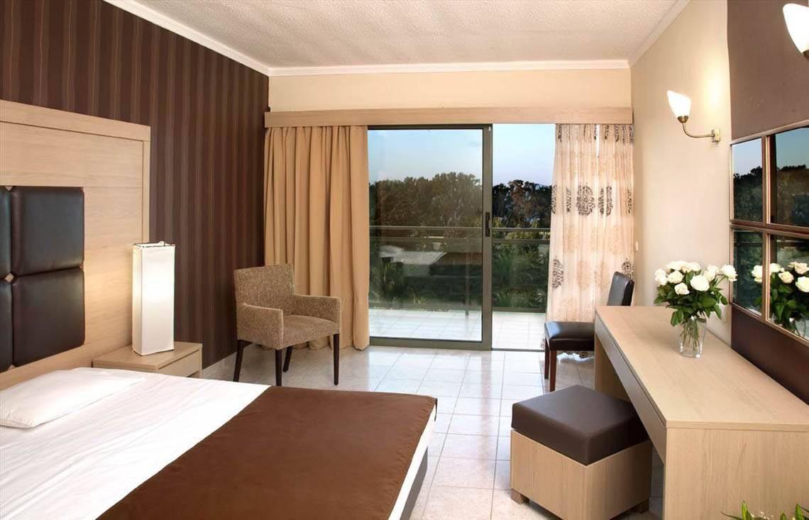 Innenansicht eines Hotelzimmers im Kipriotis Hippocrates Hotel mit Bett, Sesseln, Schreibtisch und Terrassentür.