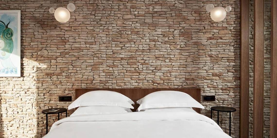 Schlafzimmer im Myconian Naia Hotel mit Steinwand und weißen Bettlaken.