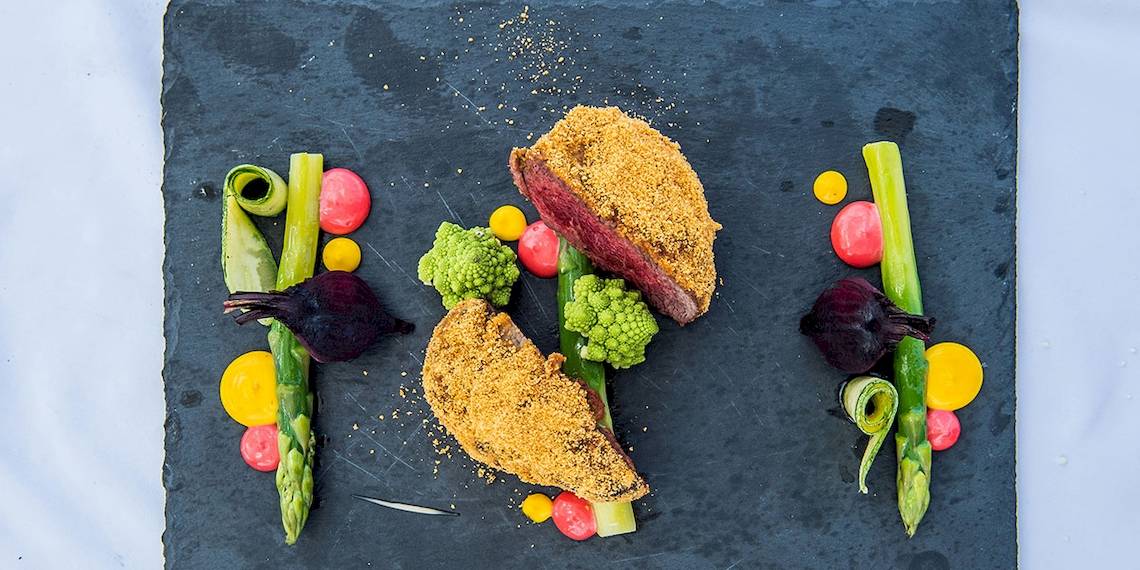 Foto eines Gourmetgerichts von Myconian Naia Hotel mit Steak, Gemüse und Beilagen auf schwarzem Teller.