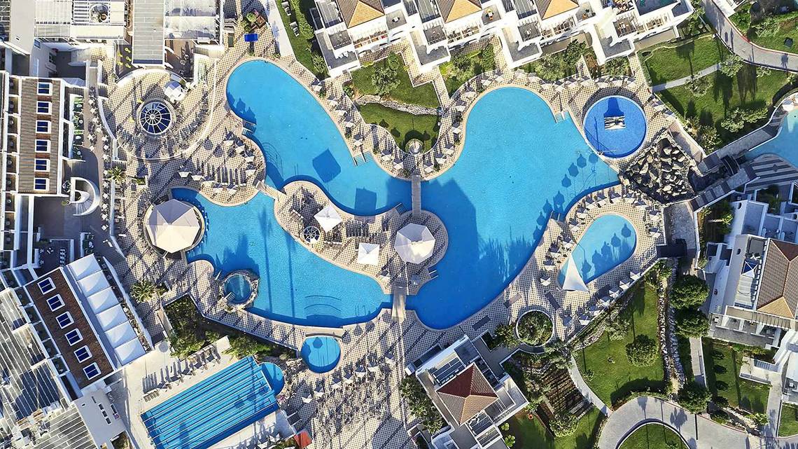 Luftaufnahme des Swimmingpools im Atlantica Marmari Palace Hotel mit mehreren Becken und Sonnenliegen.