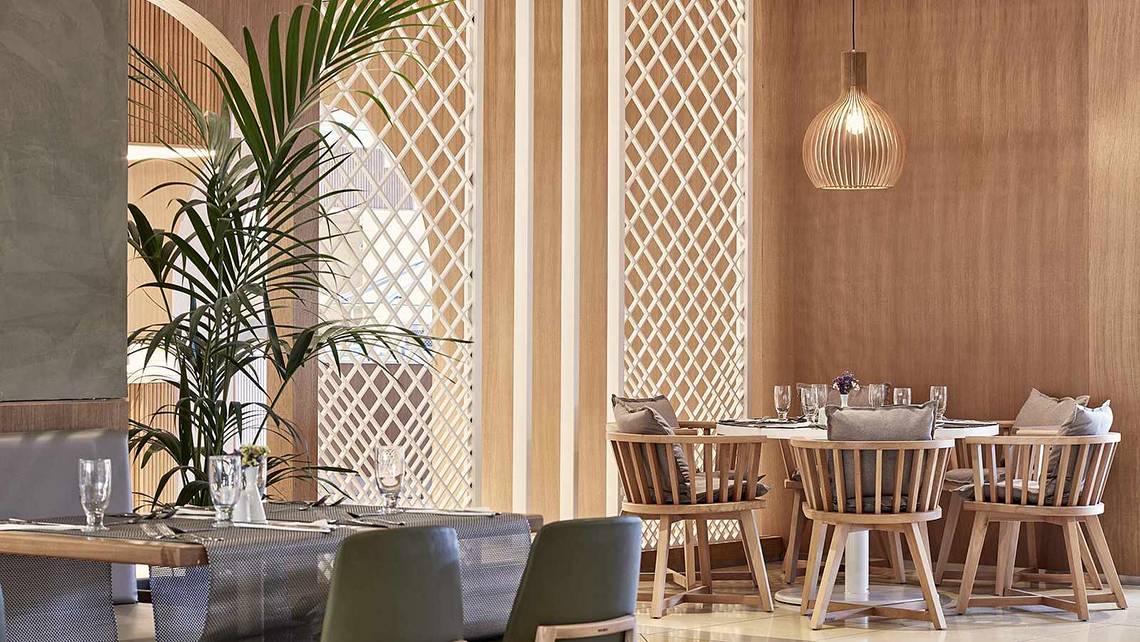 Restaurant-Innenansicht des Atlantica Marmari Palace mit Holzmöbeln, Tisch, Stühlen, Pflanzen und Pendelleuchte.