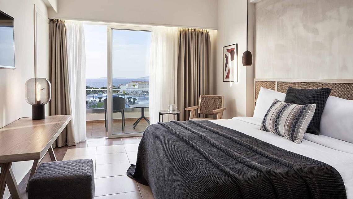Hotelzimmer des Atlantica Marmari Palace mit Blick auf den Ozean, inklusive Bett, Schreibtisch und Balkon.