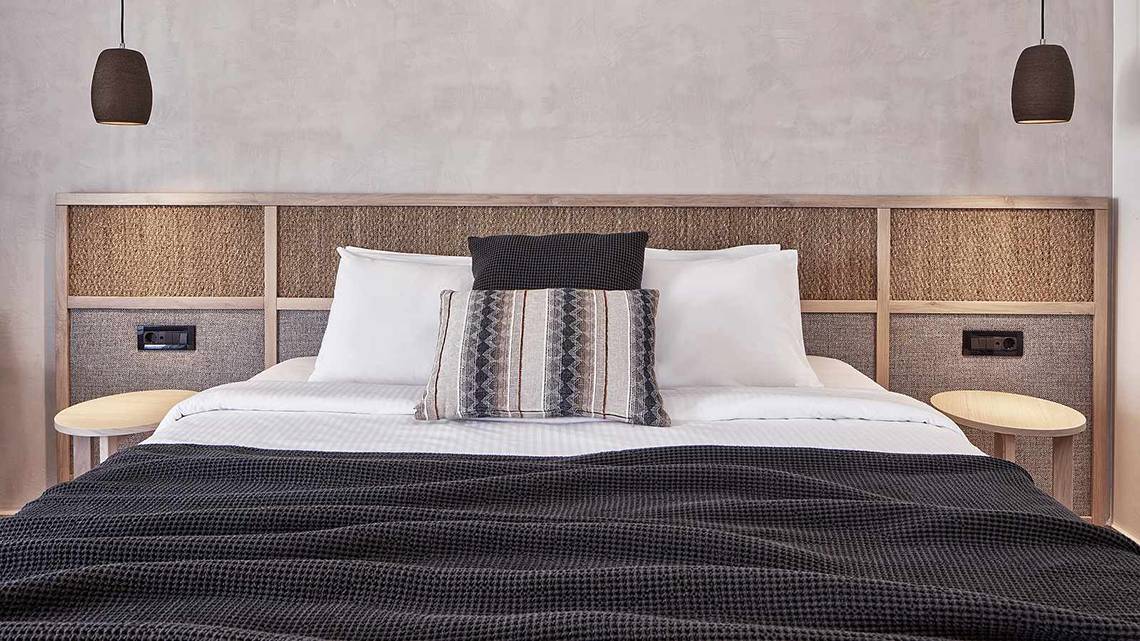 Ein modernes Zimmer im Atlantica Marmari Palace Hotel mit einem stilvollen Bett und weißen Kissen.