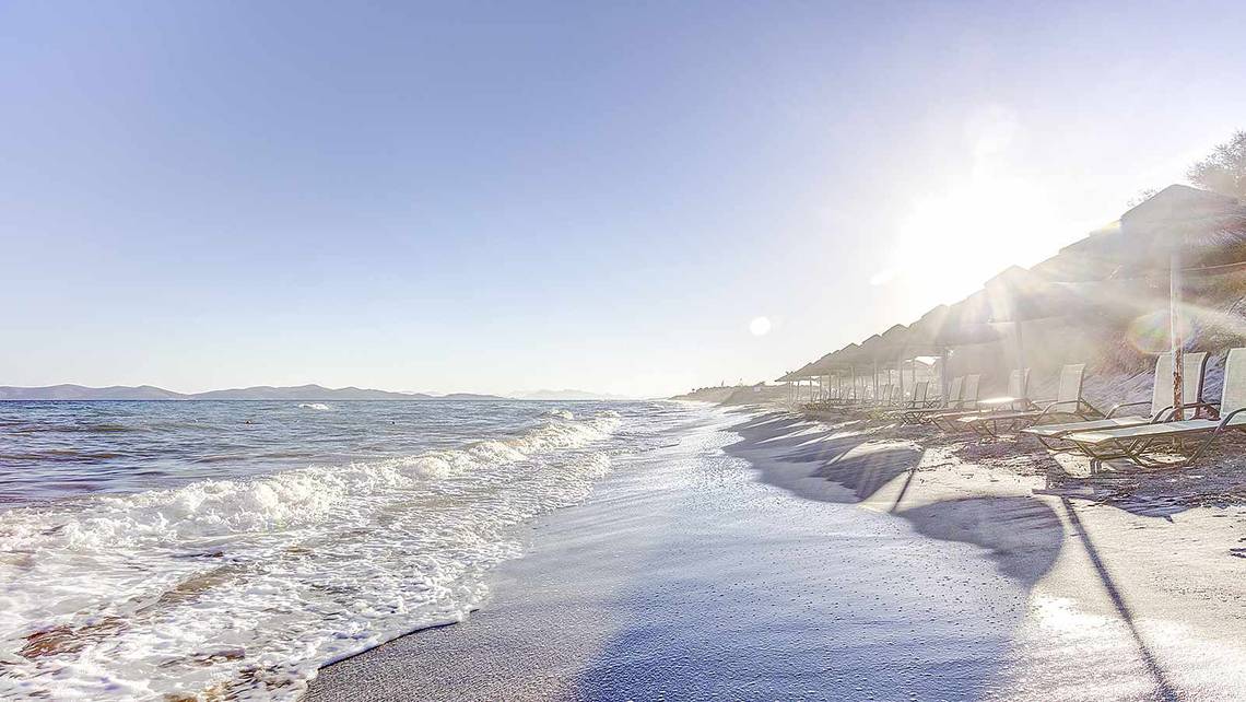 Strandszene mit Sonnenliegen und Sonnenschirmen am Meer, klares Wetter.