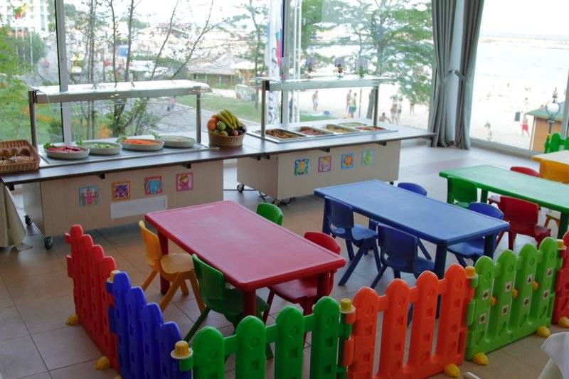 Kinderspielzimmer im Sentido Golden Star Hotel mit bunten Tischen, Stühlen und einem Blick auf das Meer.