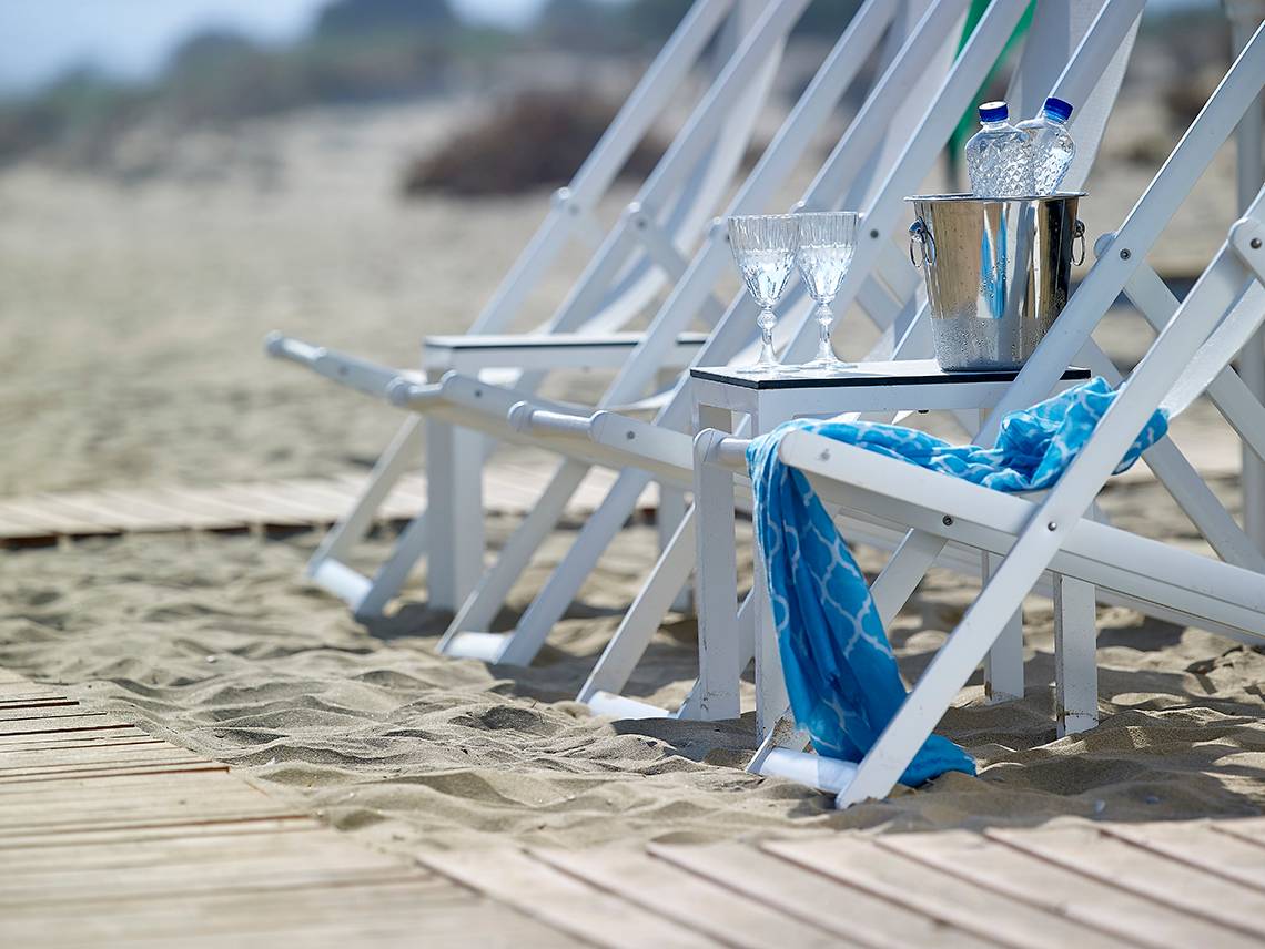 Weiße Stühle am Strand mit Eiskühler und Gläsern im Anemos Luxury Grand Resort