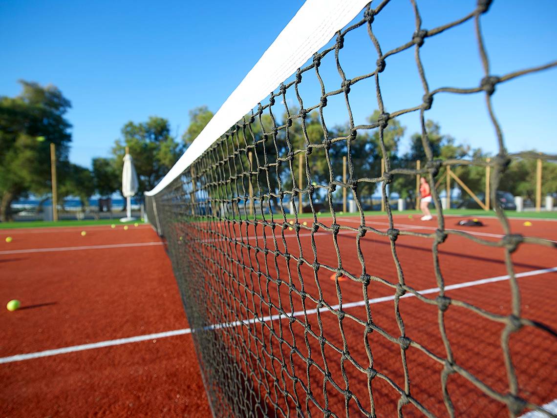 Tennisnetz auf einem roten Platz mit mehreren Tennisbällen im Hintergrund.