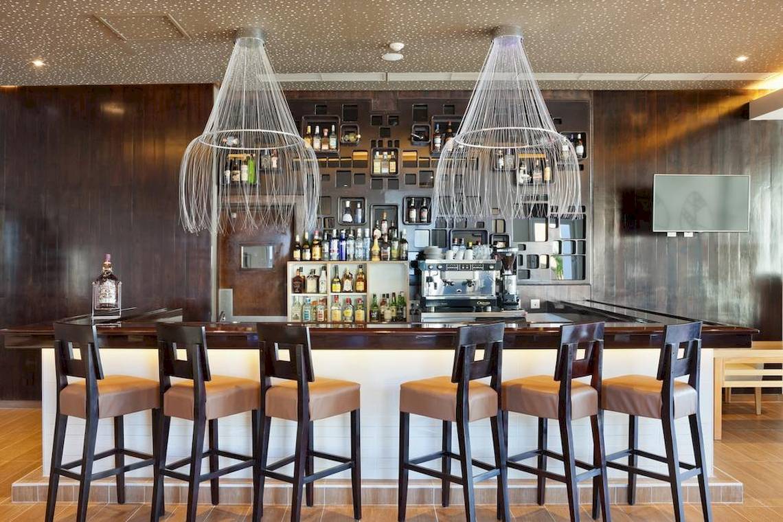 Innenansicht der Bar im Playa Vista Azul Varadero Hotel mit Barhockern, Flaschen und zwei großen Kronleuchtern.