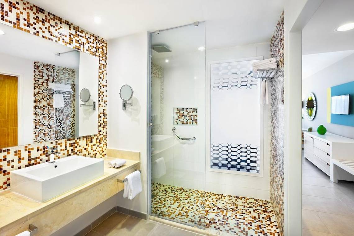 Badezimmer im Playa Vista Azul Hotel in Varadero mit gefliester Wand, Dusche und Waschbecken.