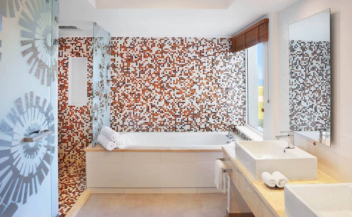 Ein Badezimmer mit einer Badewanne und einer braun-weiß gemusterten Fliesenwand.