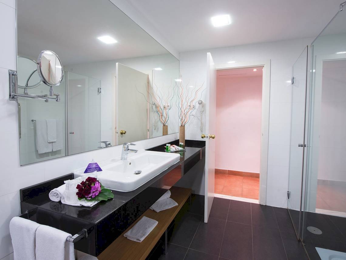 Badezimmer im Fuerteventura Princess Hotel mit Spiegel, Waschbecken und offenen Türen zur Dusche.
