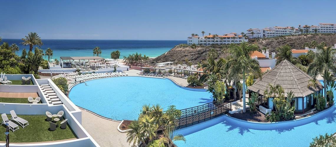 Luftaufnahme des Swimmingpools des Fuerteventura Princess Hotels mit Sonnenliegen und Blick auf das Meer.