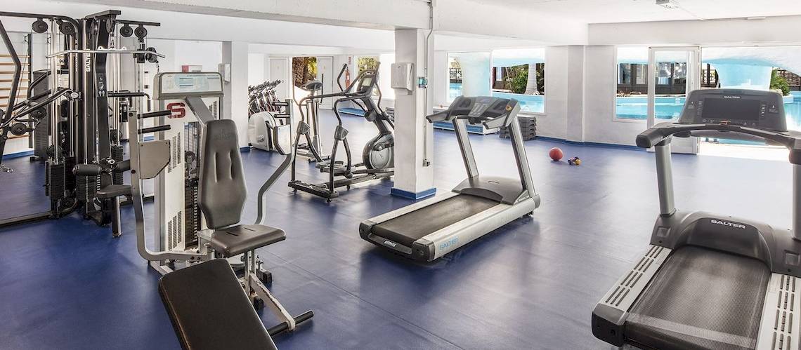 Fitnessstudio im Fuerteventura Princess Hotel mit verschiedenen Geräten und Blick auf den Pool.