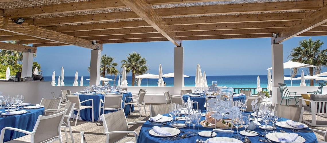 Außenbereich des Fuerteventura Princess Hotels mit blauen Tischen und Stühlen, Blick auf das Meer.