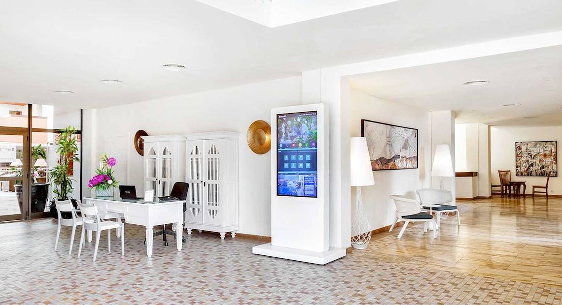 Empfangsbereich des Occidental Jandia Royal Level Hotels mit einem Tisch, Stühlen, Fernseher und Dekor.