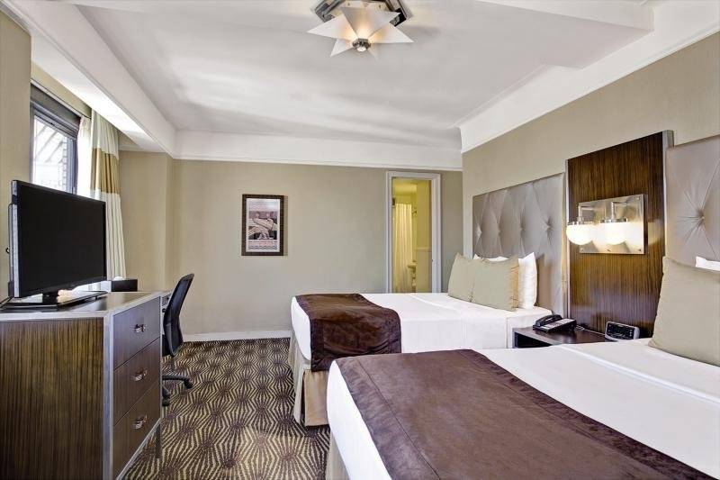 Doppelbett-Zimmer im New Yorker Hotel mit Fernseher, Schreibtisch und Nachttischen.
