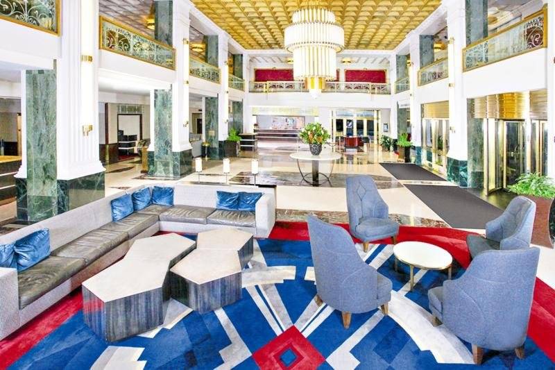 Lobbybereich des New Yorker Hotels mit blauen Stühlen, einer großen Couch und einem großen Teppich.