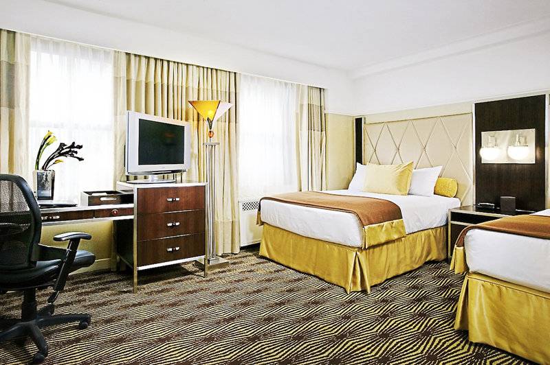 Zimmer im New Yorker Hotel mit zwei Betten, Schreibtisch, Stuhl und Fernseher.