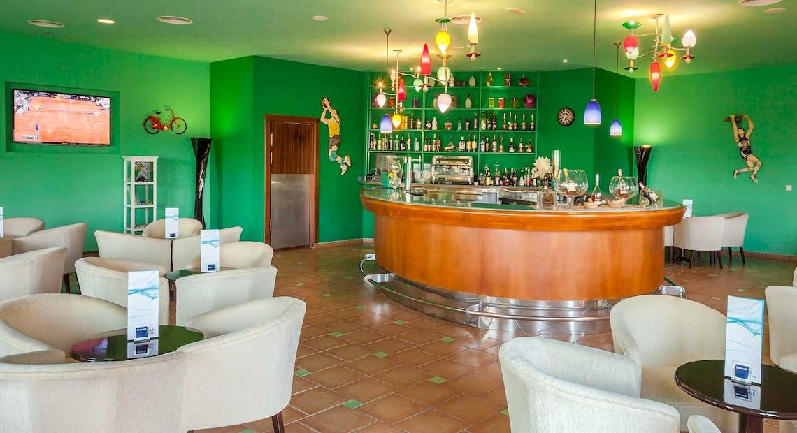 Lobby-Bar des Occidental Jandia Royal Level mit grünen Wänden, Bartheken, Kronleuchtern und Sitzbereichen.