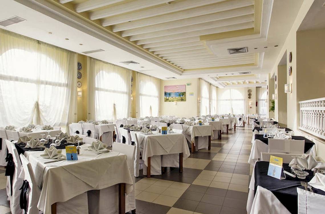 Innenansicht des Restaurants im Calimera Yati Beach Hotel mit gedeckten Tischen und Fenstern.