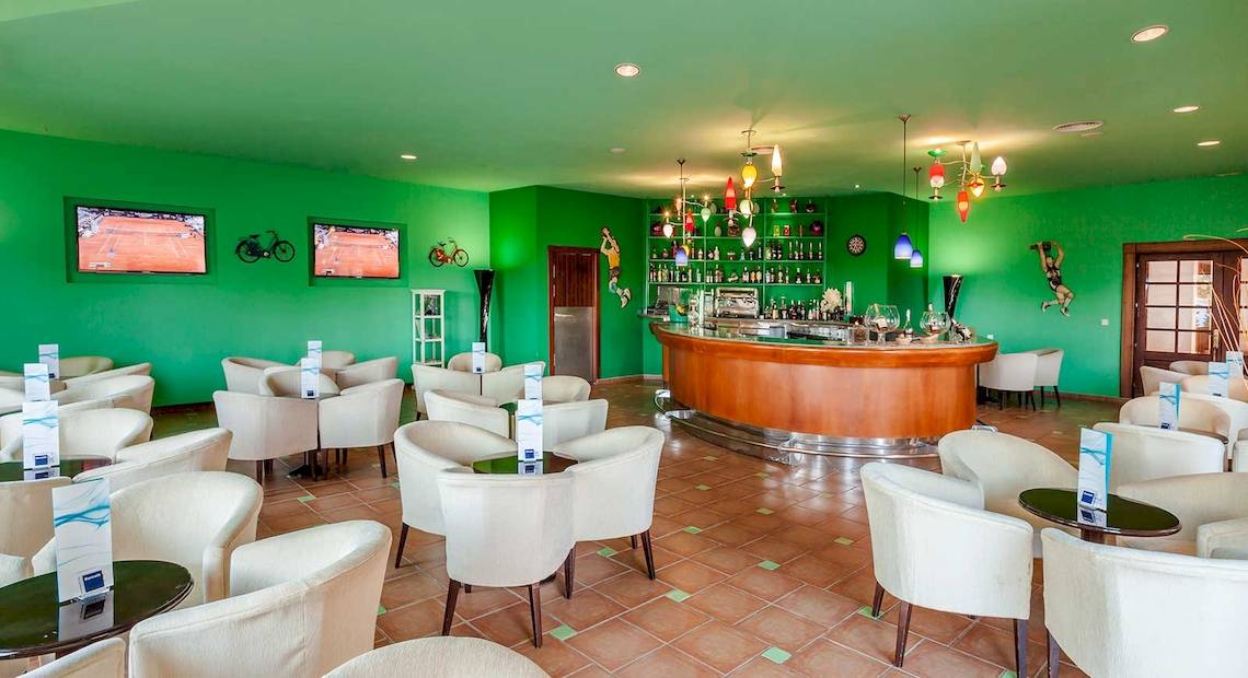 Cocktail-Bar im Occidental Jandia Royal Level Hotel mit grünen Wänden, weißen Stühlen und einer Theke.