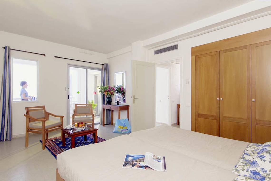 Interieur eines Zimmers im Calimera Yati Beach Hotel mit Bett, Möbeln, Fenster und Blick auf den Garten.