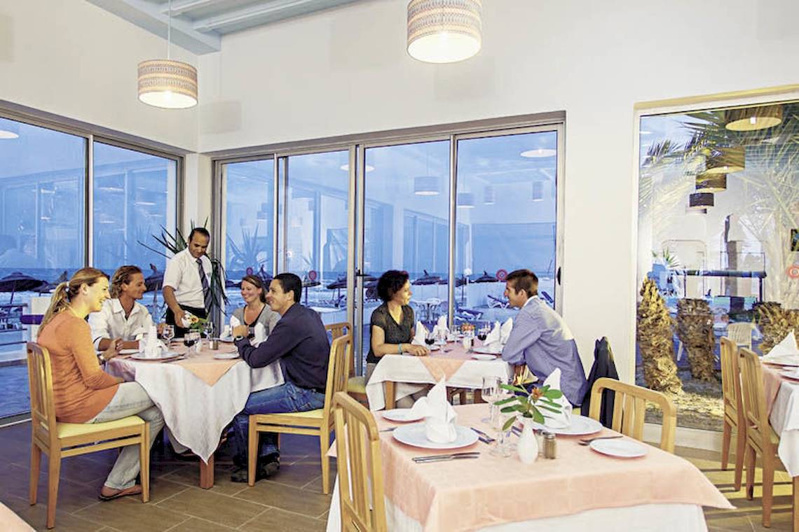 Innenansicht des Restaurants im Calimera Yati Beach Hotel mit Gästen an Tischen und einer Aussicht auf den Strand.