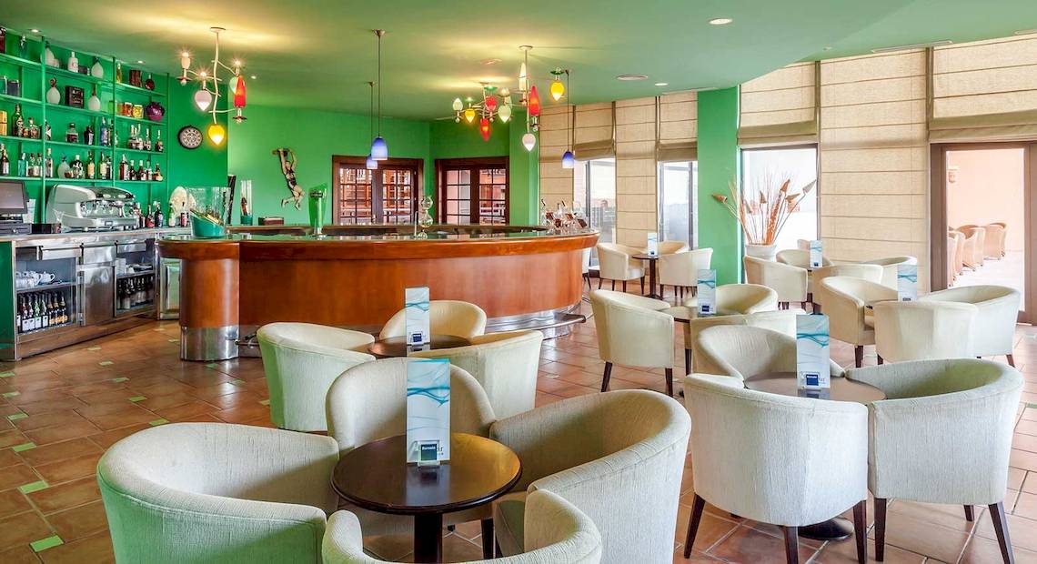 Bar im Occidental Jandia Royal Level Hotel mit grünen Wänden und weißen Stühlen.