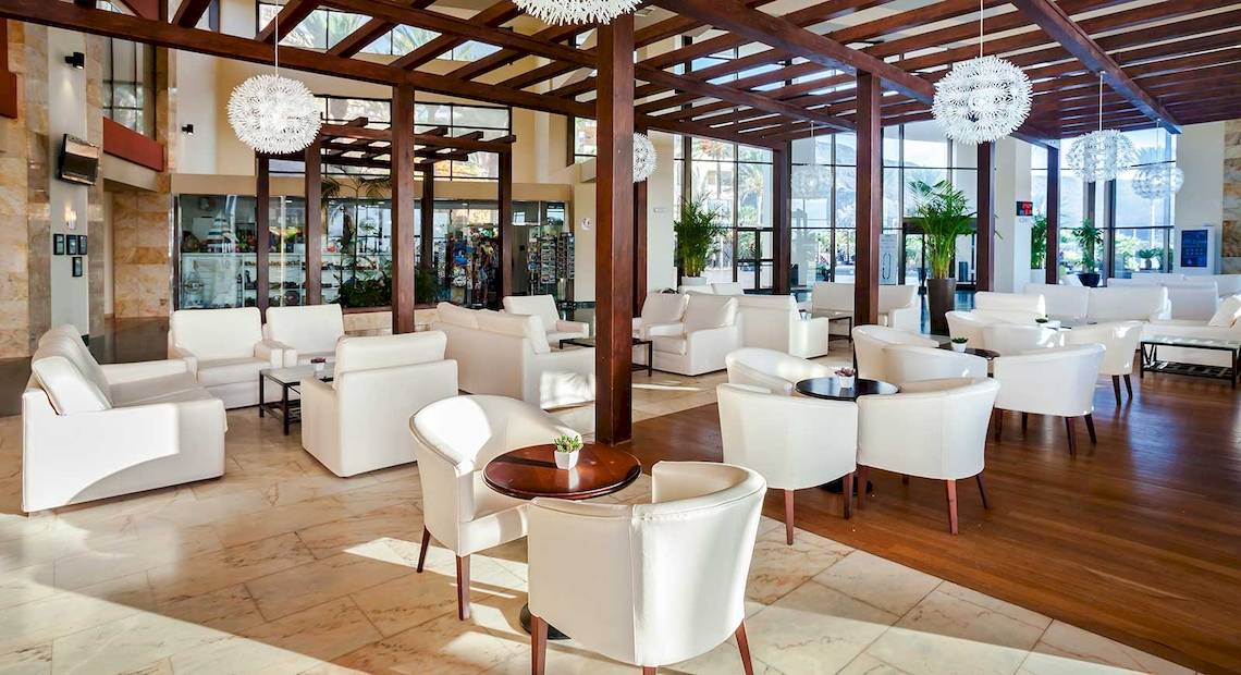 Ein Hotellobby mit weißen Sofas, Holzboden und modernen Kronleuchtern.