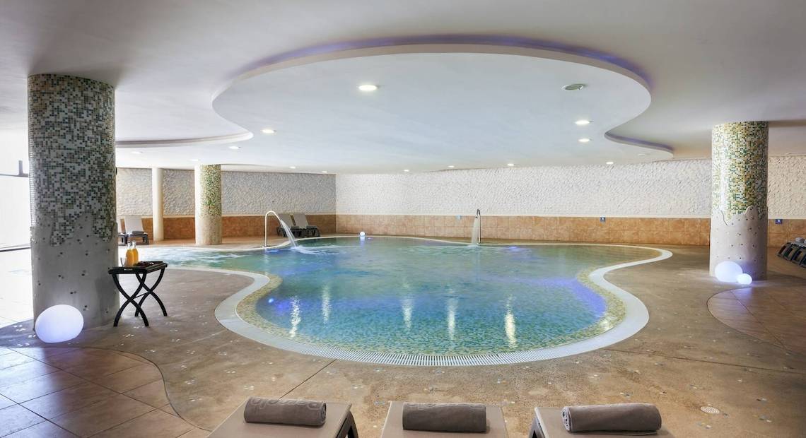 Innenpool des Occidental Jandia Mar Hotels mit Loungeliegen und Wasserfontänen.