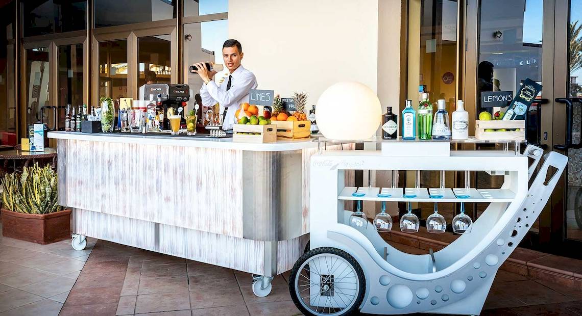 Ein Barwagen vor dem Occidental Jandia Mar Hotel mit verschiedenen Getränken und Früchten.