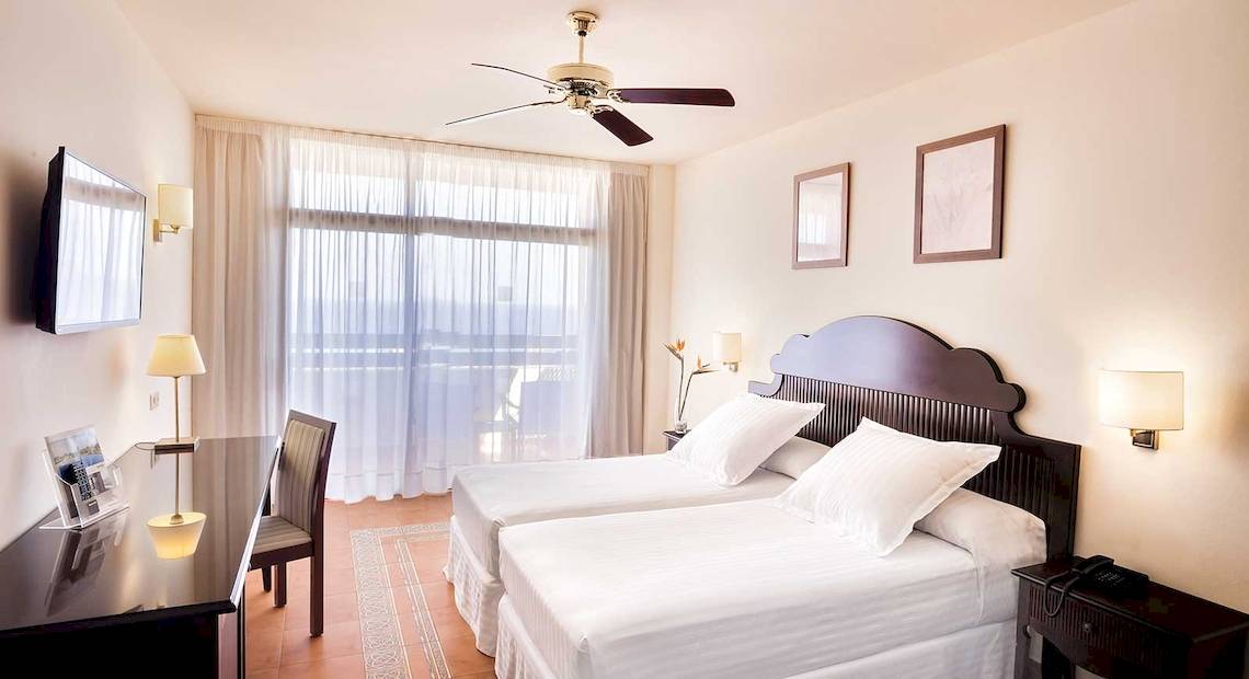 Zwei-Betten-Zimmer im Occidental Jandia Mar Hotel mit weißen Möbeln, Deckenventilator und Fernseher.
