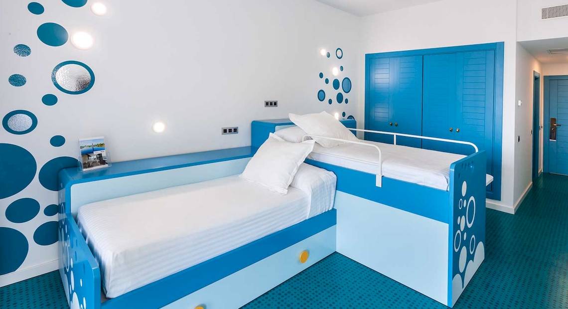 Doppelzimmer im Occidental Jandia Mar Hotel mit blauer und weißer Inneneinrichtung, zwei Betten, weißen Kissen und blauen Schranktüren.