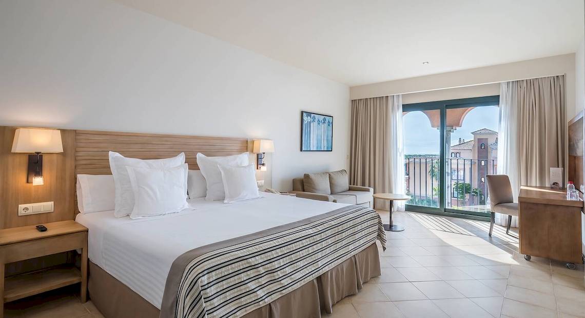 Hotelzimmer im Occidental Jandia Mar mit Balkon, Bett, Couch und Schreibtisch.