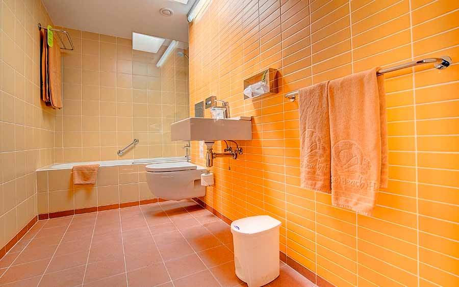 Badezimmer im SBH Monica Beach Resort mit gelben Fliesen, Badewanne und Toilette.