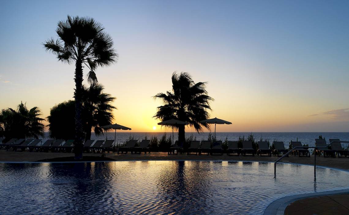 Sonnenuntergang am Pool des H10 Tindaya Hotels mit Palmen und Sonnenschirmen.