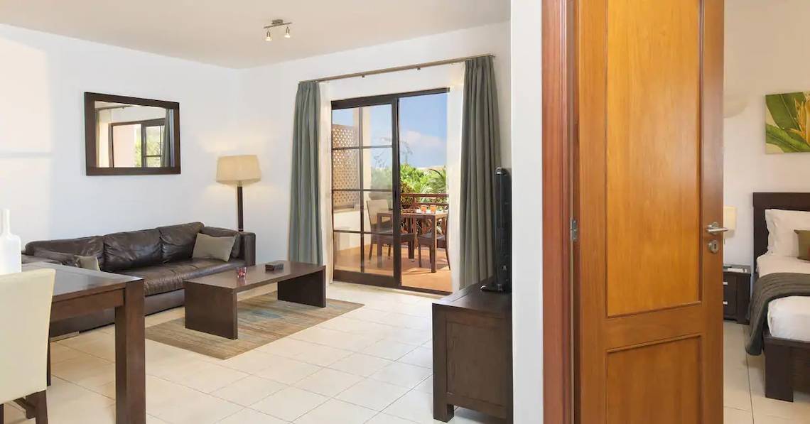 Innenansicht der Suite im Melia Tortuga Beach Hotel mit Wohnzimmer, Couch, Tisch, Lampe, Fernseher und Balkon.