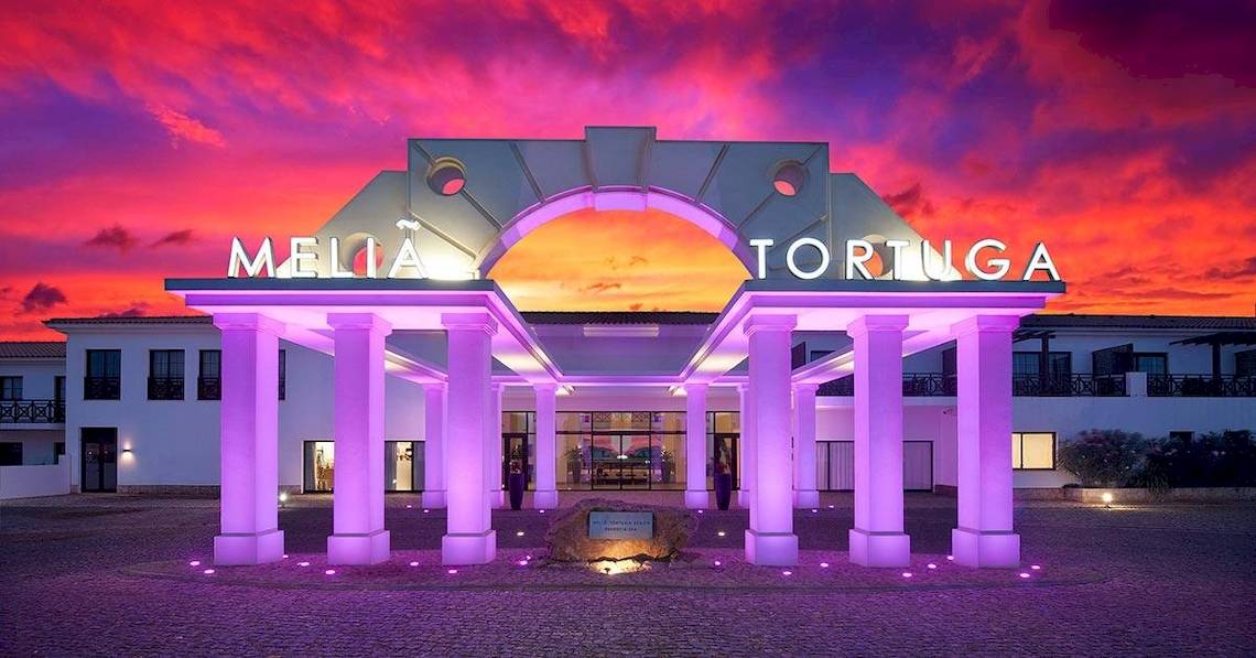 Der Eingang des Melia Tortuga Beach Hotels bei Nacht mit lila Beleuchtung und einem roten Himmel.