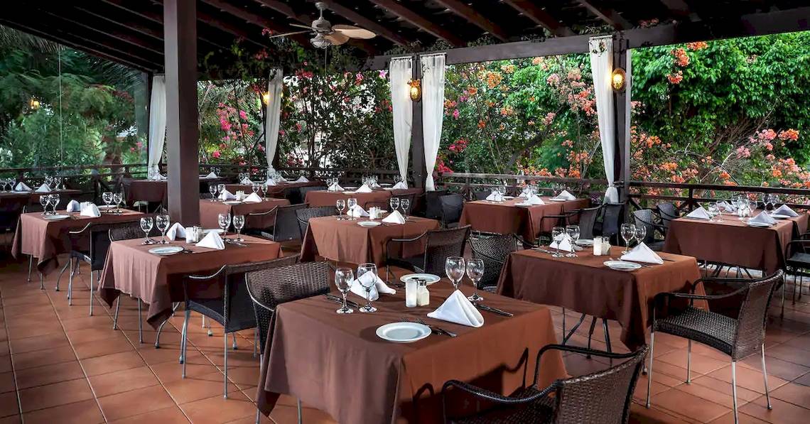 Restaurant-Terrasse des Melia Tortuga Beach Hotels mit braunen Tischen und Stühlen, umgeben von Pflanzen.