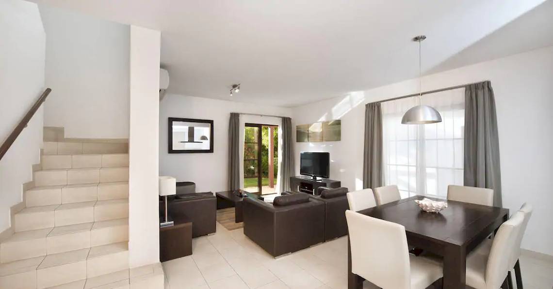 Wohnbereich des Melia Tortuga Beach Hotels mit weißen Wänden, einer Treppe, einem Sofa und einem Fernseher.
