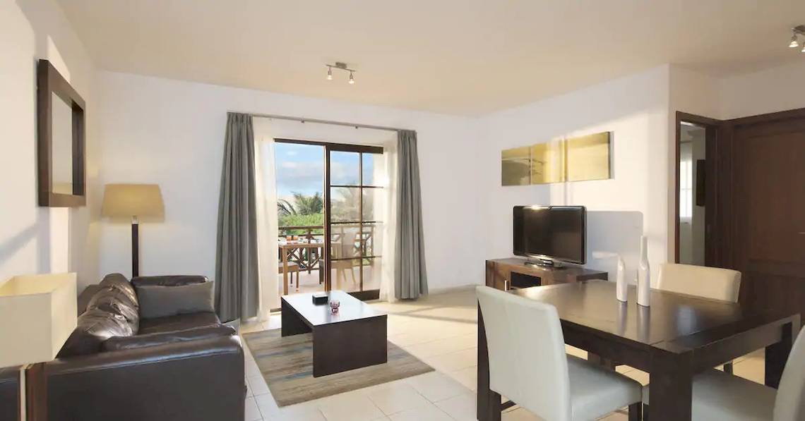 Wohnbereich des Melia Tortuga Beach Hotels mit Couch, Tisch, Fernseher und Balkonzugang