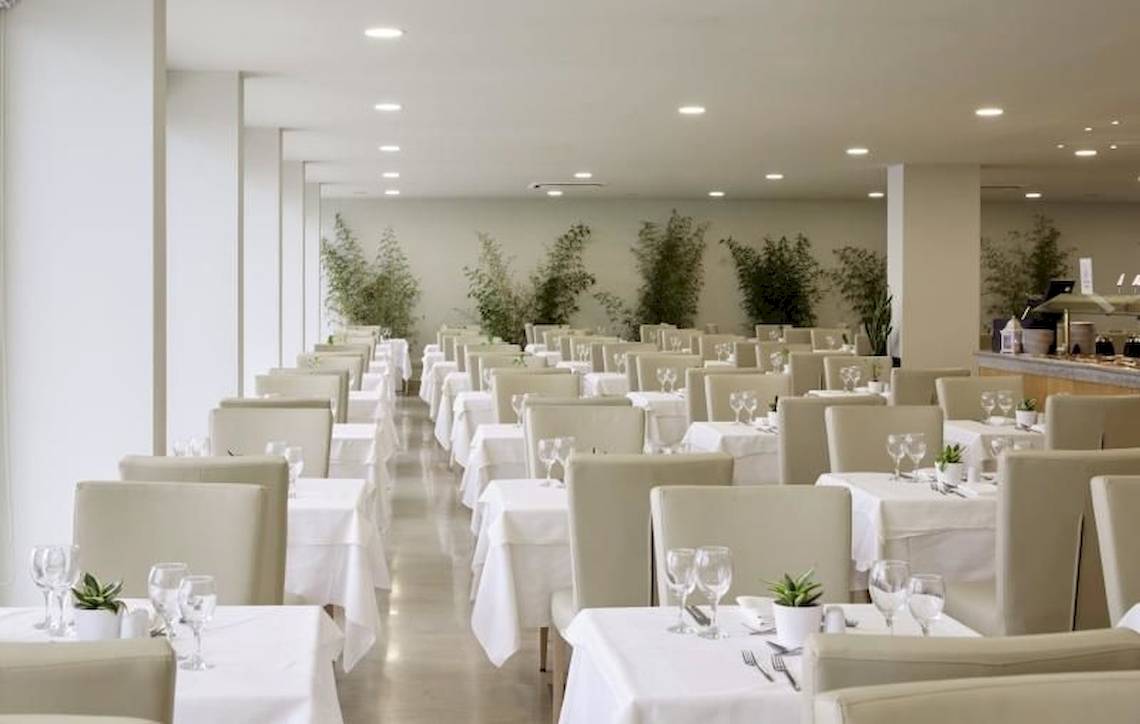 Restaurant des Alkyna Lifestyle Beach Resorts mit weißen Tischen und Stühlen, Pflanzen und Deckenlampen.