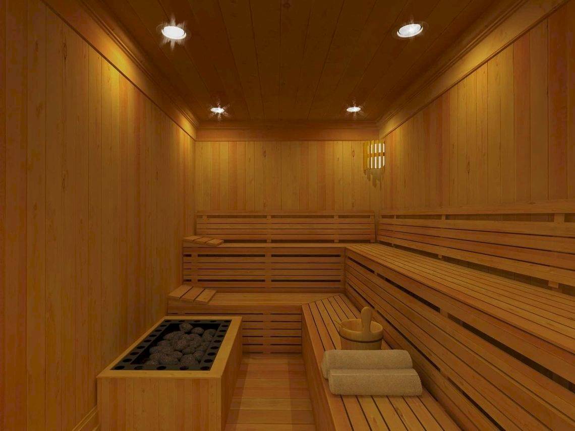 Innenansicht einer Holzsauna im Alkyna Lifestyle Beach Resort mit Holzbänken, einem Feuerbecken und hellen Beleuchtungskörpern.
