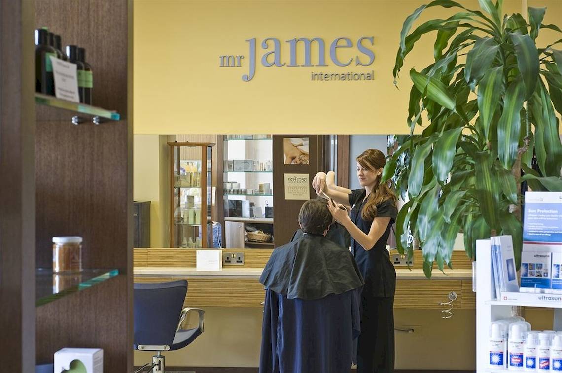 Friseursalon mit Frau, die einem Mann die Haare schneidet, Schild mit Mr. James International.