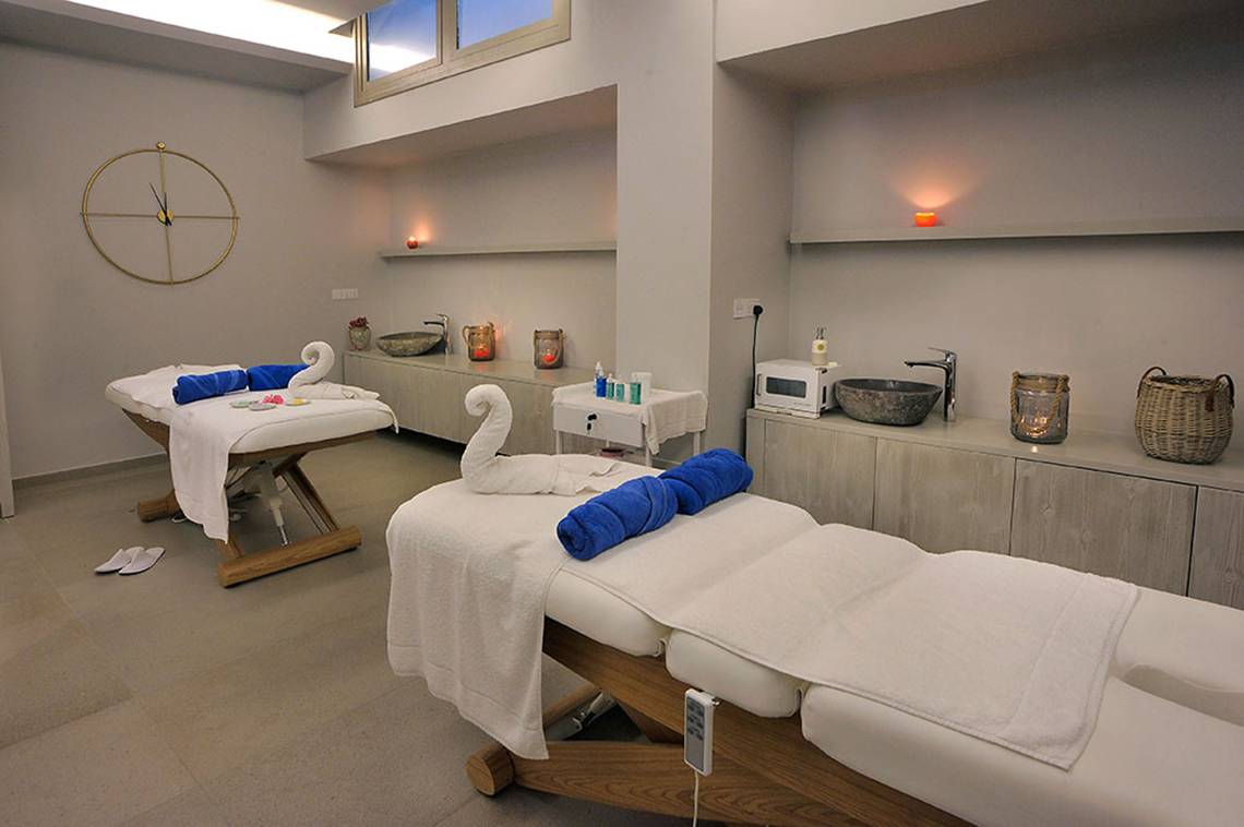 Massageraum im Nelia Beach Hotel & Spa mit zwei Massagetischen, weißen Handtüchern und blauen Kissen.