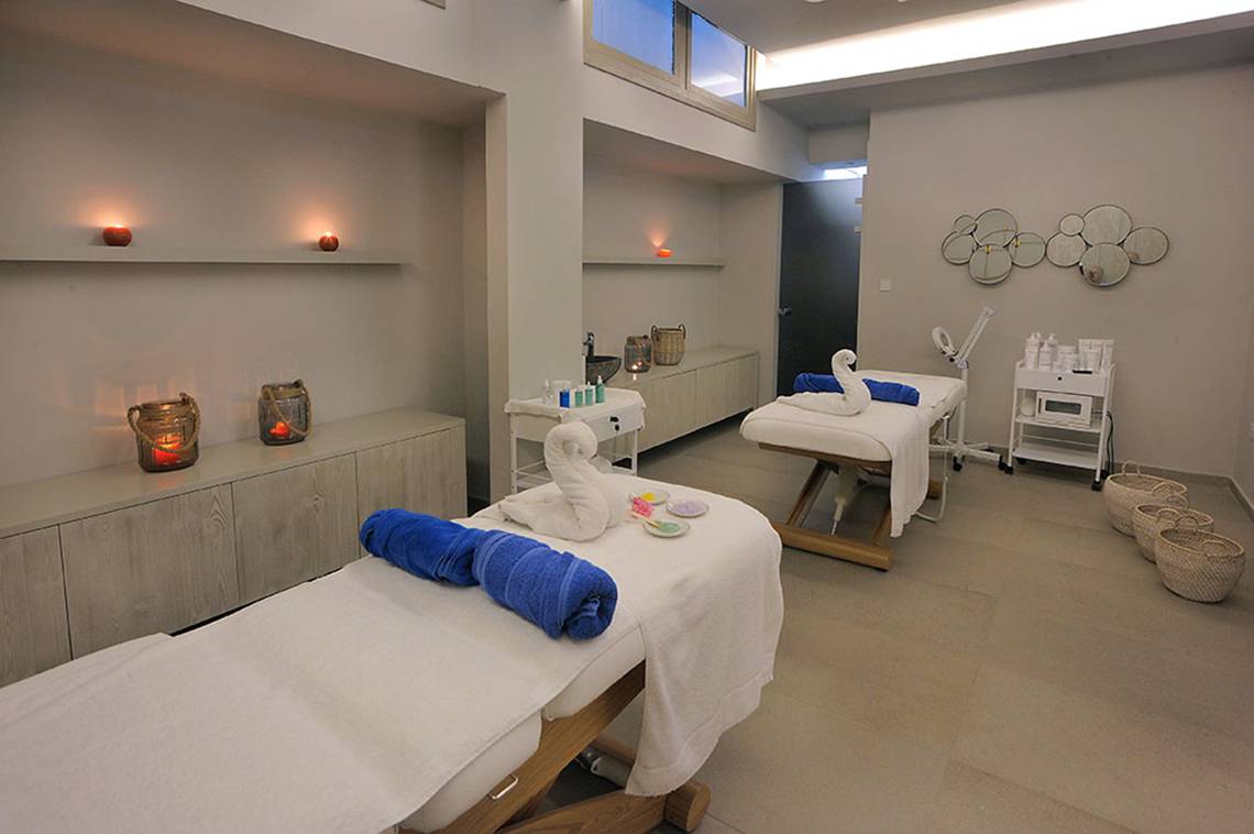 Spa-Massageraum im Nelia Beach Hotel & Spa mit zwei Massagetischen, blauen Handtüchern und dekorativen Elementen.