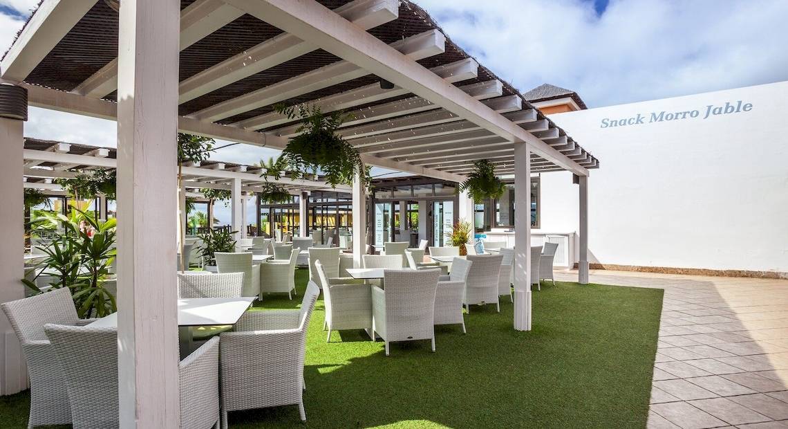 Terrasse des Occidental Jandia Playa Hotels mit Tischen und Stühlen unter einer Laube.
