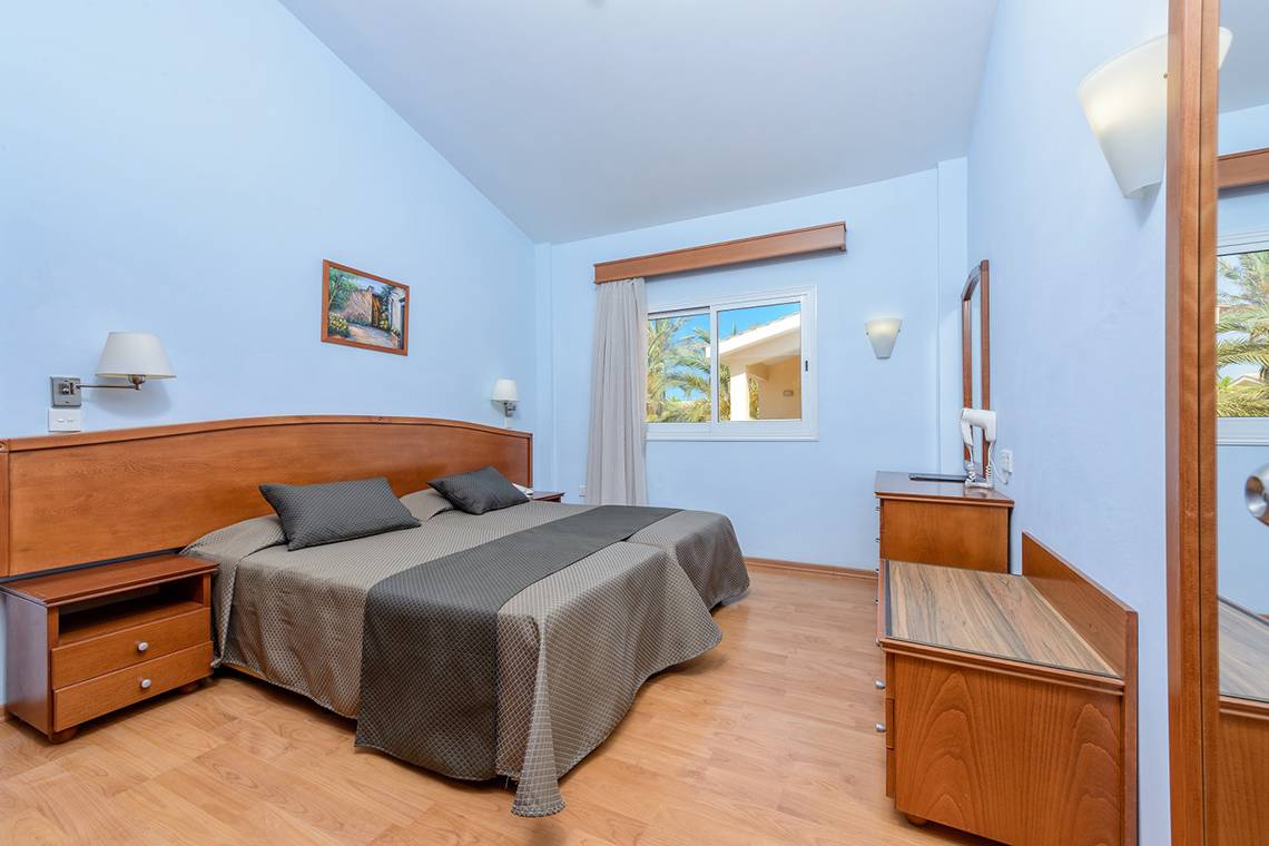 Ein modernes Hotelzimmer im Tasia Maris Sands mit Doppelbett, Nachttischen und Badezimmerspiegel.