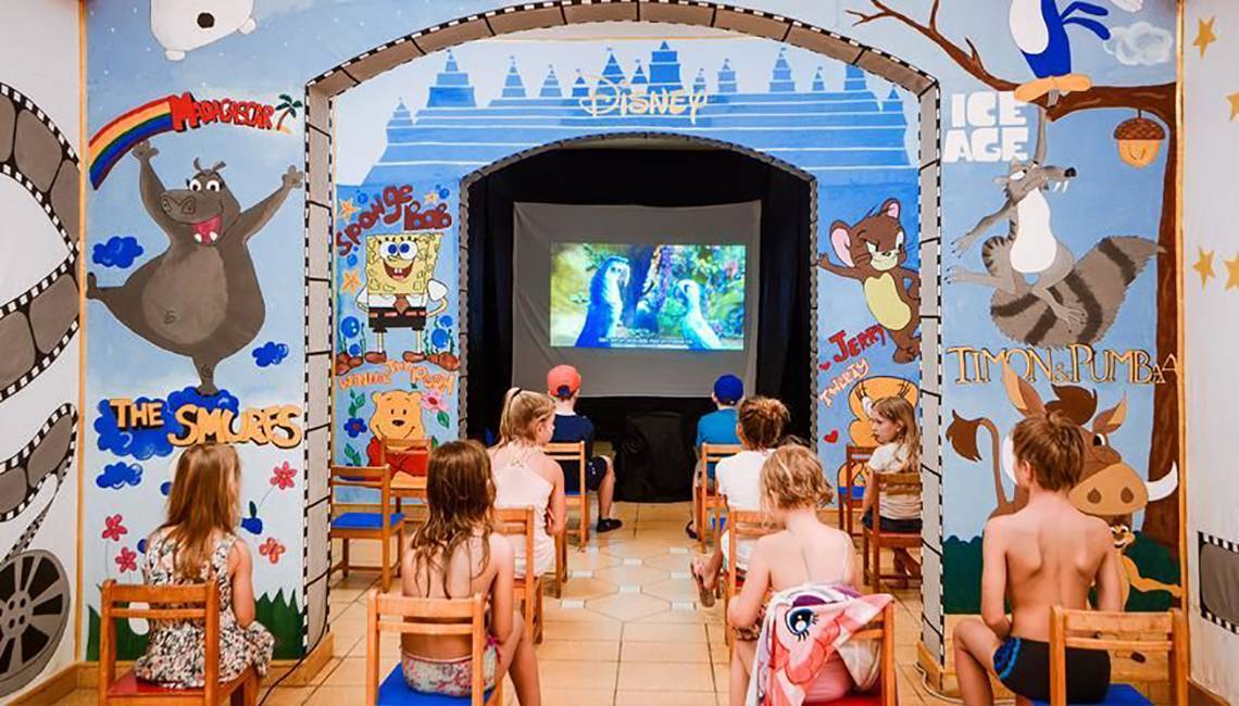 Kinder sitzen in einem Kinobereich im Jaz Lamaya Resort, der mit Disney-Charakteren wie Micky Maus und Winnie Puuh dekoriert ist.